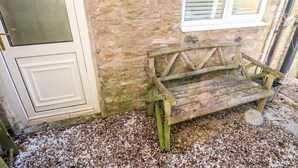 A stone building with a wooden bench outside, a door, and a window with shutters. - Kings Cottage (Alston)