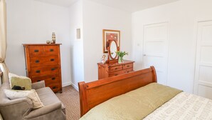 A bedroom with a bed, a wooden dresser, a chair, and a dresser with a mirror. - Kings Cottage (Alston)