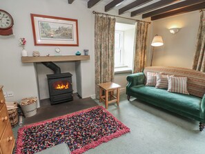 A cozy living room with a fireplace, a green sofa, a wooden table, and a colorful rug. - Bill's Place (Leyburn)