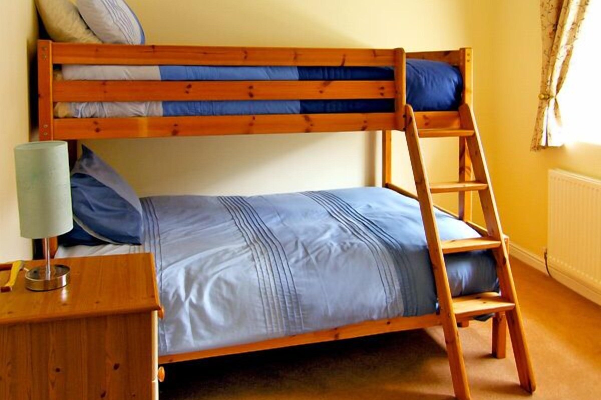 A bunk bed with a ladder, a bedside table with a lamp, and a window with curtains.