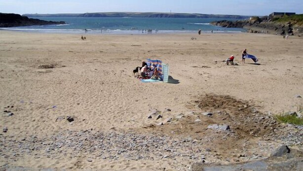 A beach with a few people, a lifeguard tower, and a rocky area.