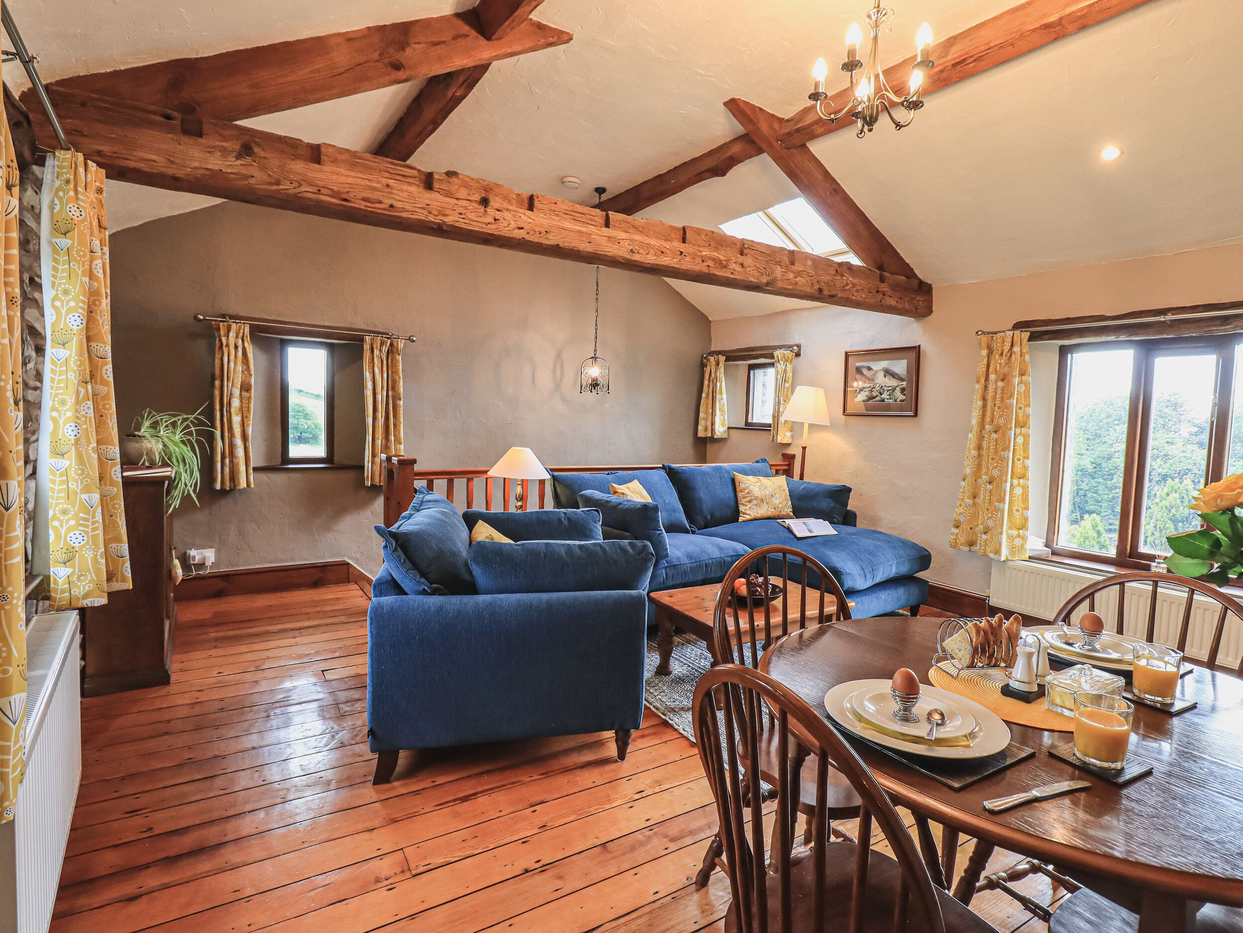 A cozy living room with a blue sofa, wooden dining table, and a chandelier.