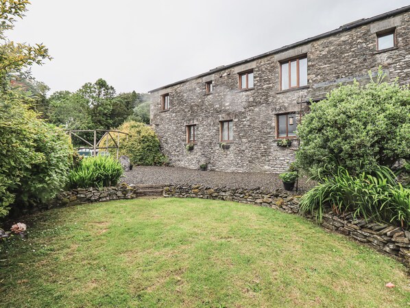 A stone building with a grassy courtyard, surrounded by various plants and trees. - Hollins Farm Barn (Kendal)
