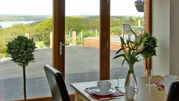 A dining area with a table set for two, a view of a lake, and potted plants.