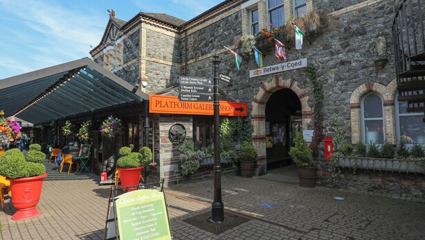 En historisk byggnad i sten med en skylt som visar vägen till konstgalleriet Platform Gallery Shop och kaféet Alpine Coffee Shop.
