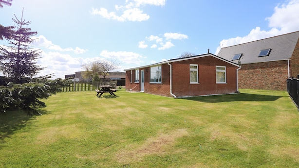 A residential property with a brick house, a lawn, and a picnic table. - Sheppard's Hut (King's Lynn)