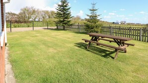 A grassy outdoor area with a picnic table and a wooden fence. - Sheppard's Hut (King's Lynn)