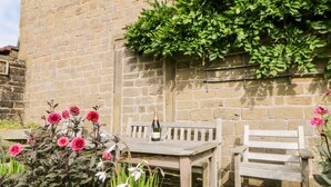 Un mur de pierres avec un banc et une table en bois, le tout entouré de fleurs.