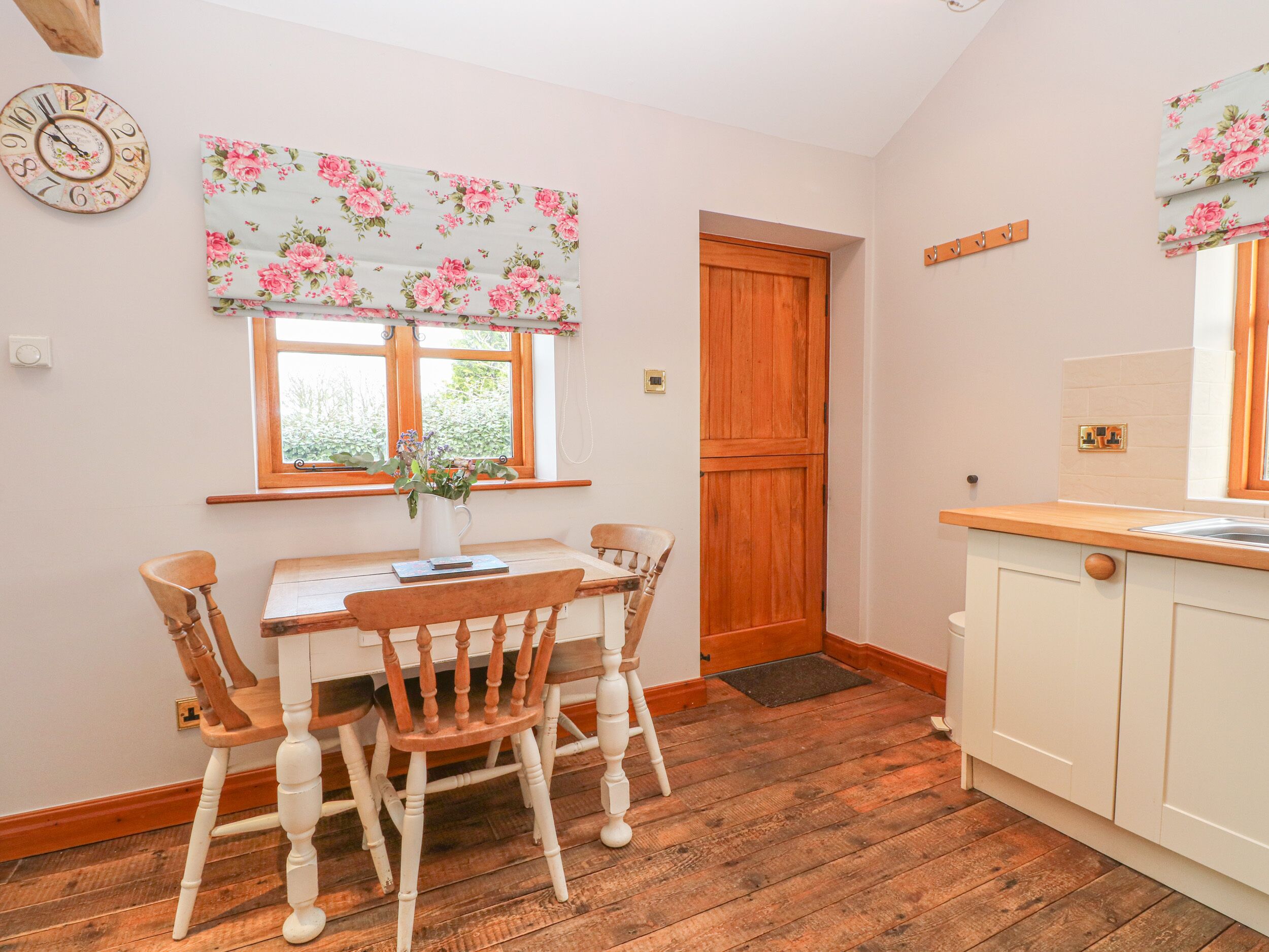 Een gezellige keuken met houten vloeren, een eettafel met stoelen, een houten deur en een raam met bloemen gordijnen.