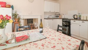 A cozy kitchen with white cabinets, a stove, and a dining table set for two with a floral tablecloth. - Wards Court 2 (Gloucester)