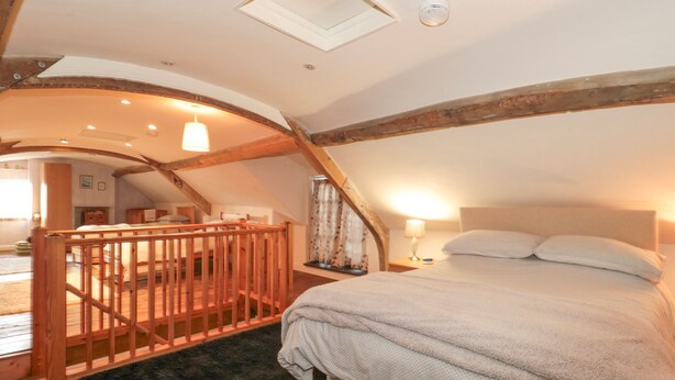 A bedroom with a large bed, wooden beams, a skylight, and a staircase leading to an upper level. - Wards Court 2 (Gloucester)