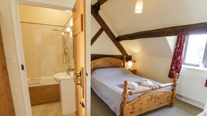 A bedroom with a wooden bed, a nightstand, a bedside lamp, and a window with curtains. - Kite's Nest (Church Stretton)
