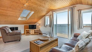 A cozy living room with a wooden ceiling, a sofa, a coffee table, and a TV. - Sail Loft (Yarmouth)