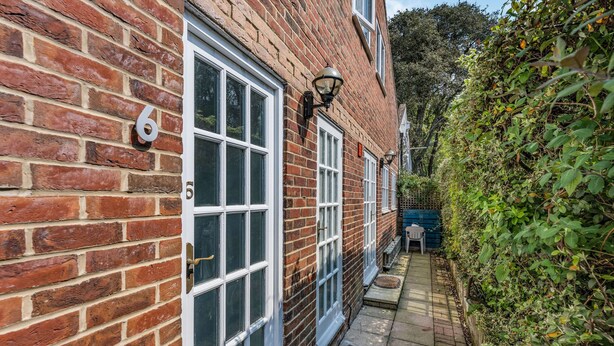 A brick house with white-framed windows and a door, a number '6' on the wall, and a pathway leading to a blue gate. - Sail Loft (Yarmouth)