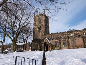A historic church with a tall clock tower, a snow-covered pathway, and a large tree in the foreground.