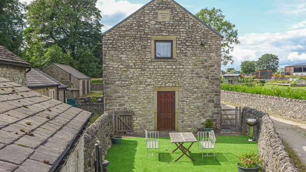 Un bâtiment en pierre avec une porte rouge, une petite pelouse et une table entourée de chaises.