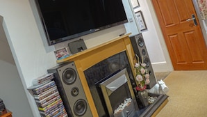Un salon doté d’un téléviseur à écran plat fixé au-dessus d’une cheminée, entouré de haut-parleurs et d’une collection de DVD.