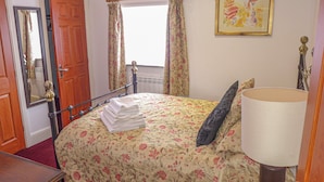 Une chambre à coucher comprenant un lit, une table de chevet, une lampe, une fenêtre avec des rideaux, une porte et un miroir.