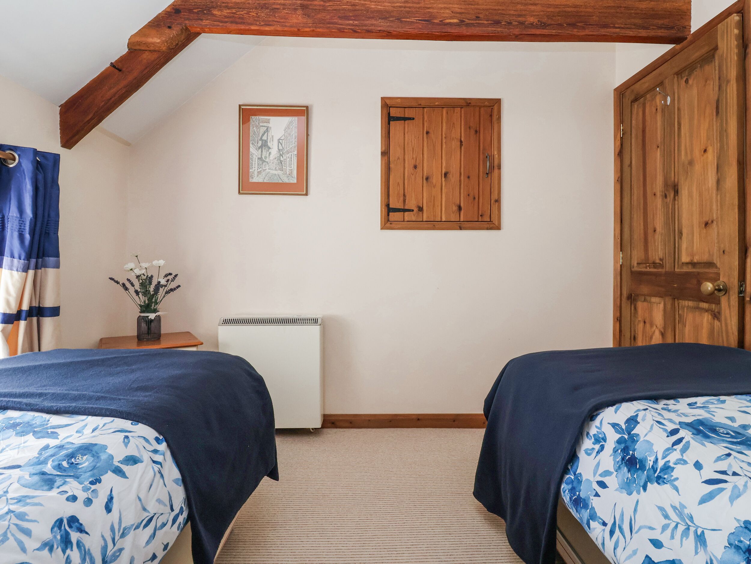 Een slaapkamer met twee bedden, een houten deur, een radiator, een ingelijst kunstwerk en een gordijn.
