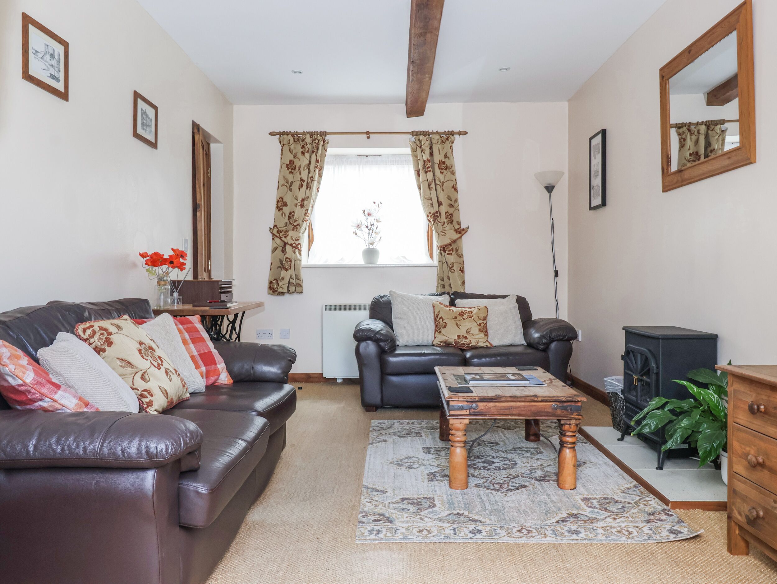 A living room with a sofa, a wooden coffee table, and a radiator. There is a window with curtains, a mirror, and a plant.