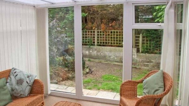 A conservatory with wicker furniture, including a sofa and chairs, and a small table. - Matlock Green (Matlock)