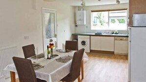 A compact kitchen with a dining area, featuring a table set for two, a washing machine, and a refrigerator. - Matlock Green (Matlock)