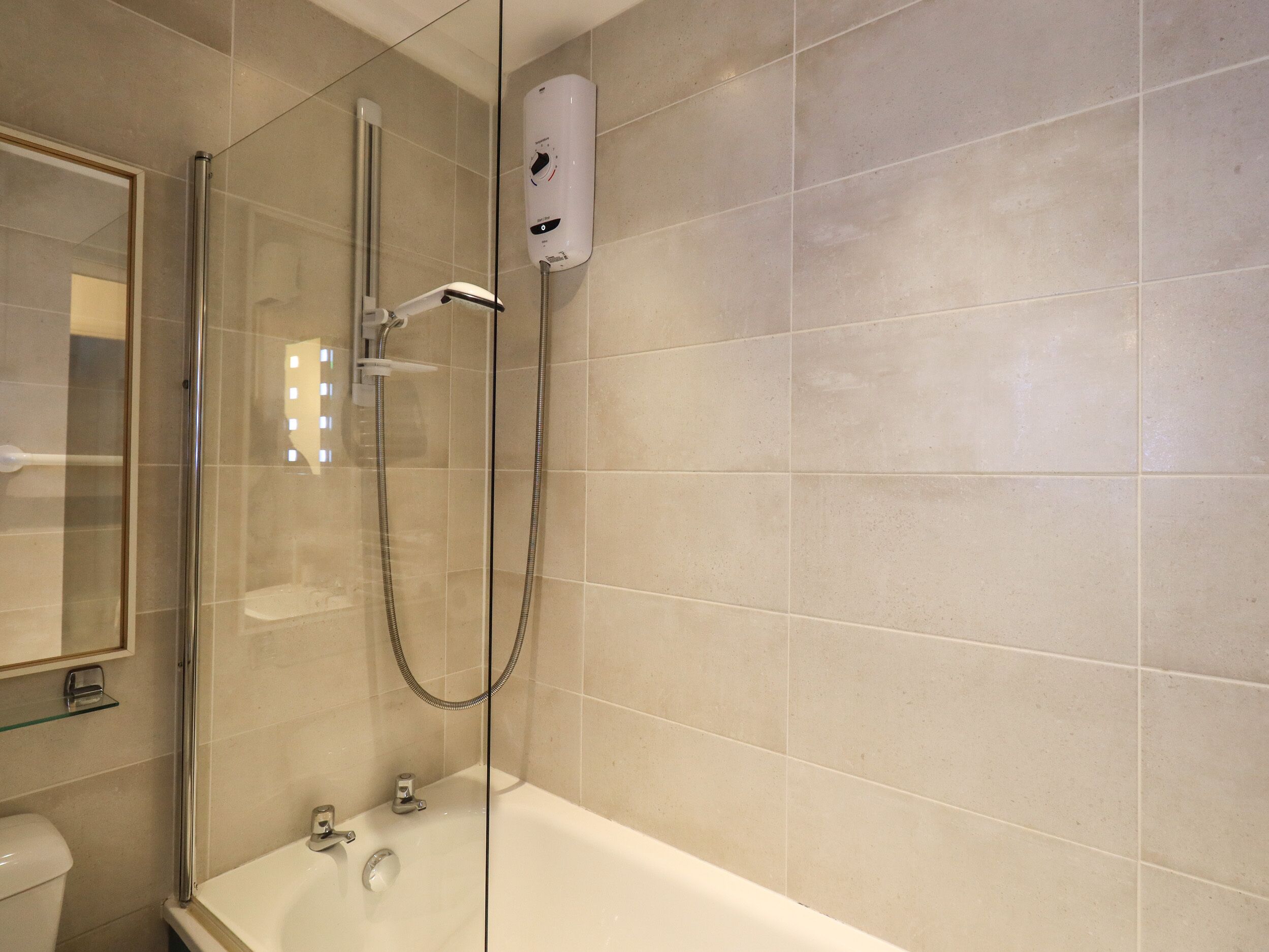 Un baño moderno con ducha envuelta en vidrio, bañera blanca y calentador de pared.