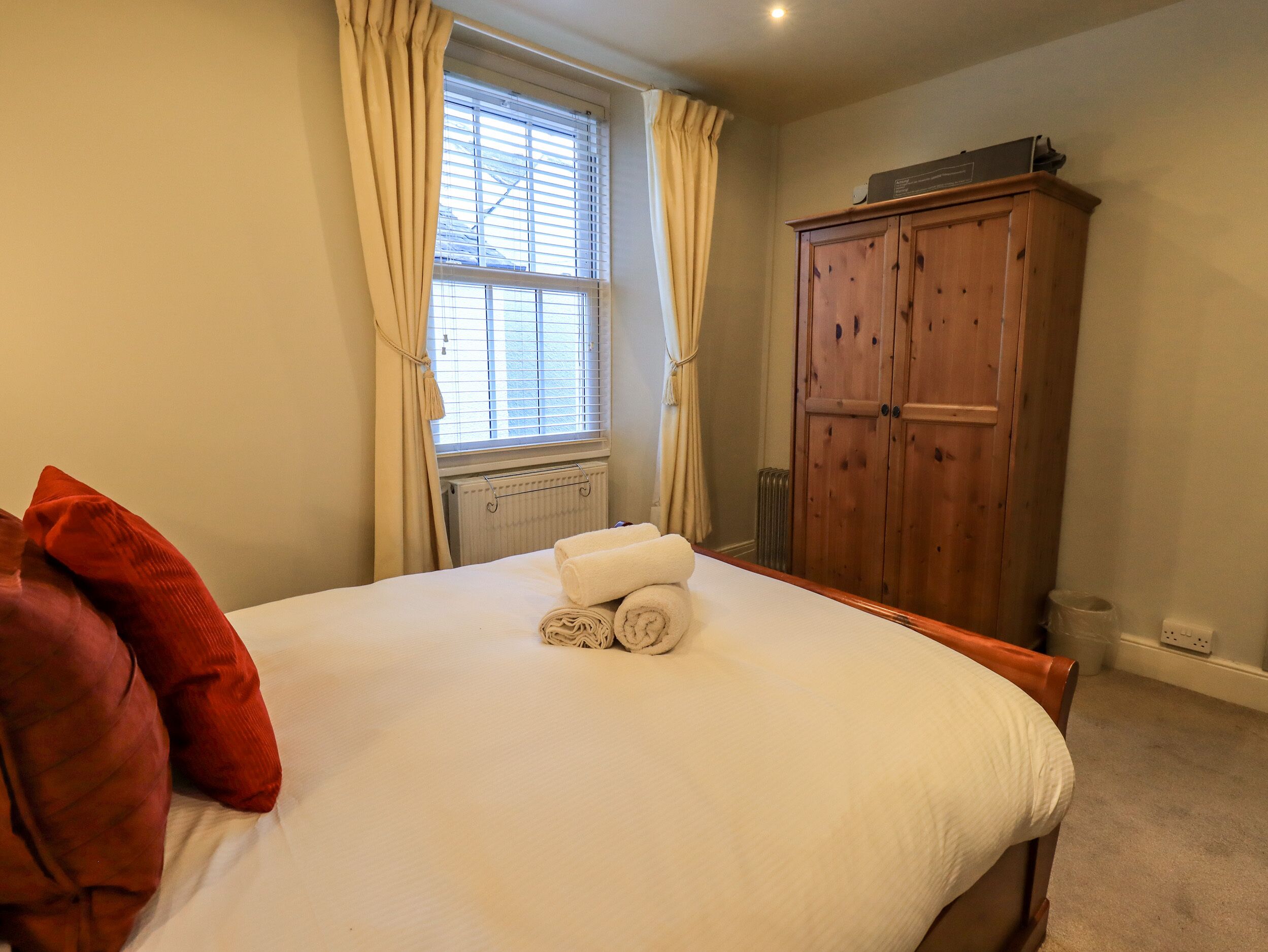 A bedroom with a bed, a radiator, a wooden wardrobe, and a window with curtains.