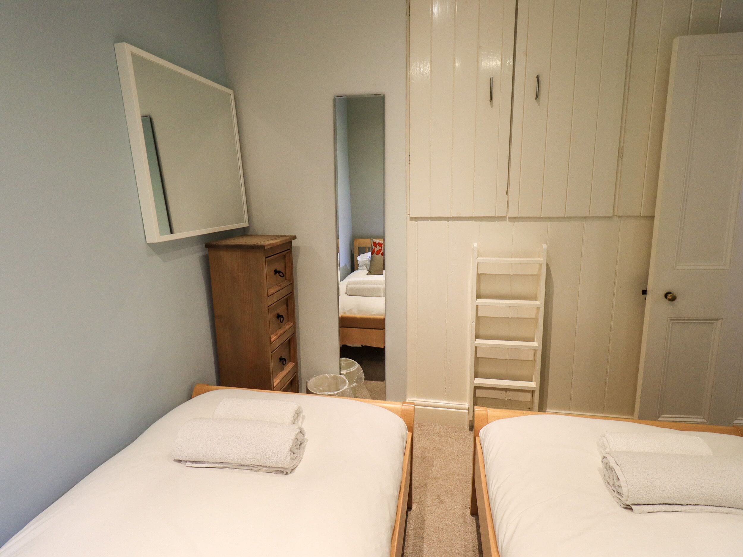 A bedroom with two beds, a wooden dresser, a white wardrobe, and a mirror on the wall.