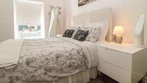 Un dormitorio con cama, mesita de noche con lámpara, espejo y vistas al exterior.