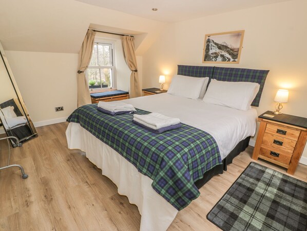 A neatly arranged bedroom with a bed, bedside tables, a mirror, and a window with curtains. - Alma Cottage (Crianlarich)