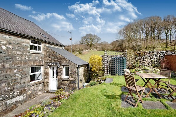 A stone house with a small garden, a wooden table and chairs, and a stone wall. - Ty Capel Jeriwsalem (Blaenau Ffestiniog)