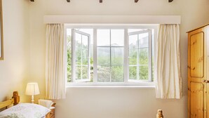 Un dormitorio con cama, mesita de noche, lámpara, armario de madera y ventana con cortinas.