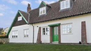 Uma casa de dois andares com uma porta verde, paredes brancas e telhado em telhas.