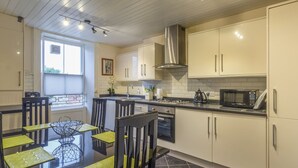 Uma cozinha moderna com armários brancos, chão de azulejos pretos e uma área de refeições com mesa e cadeiras de vidro.