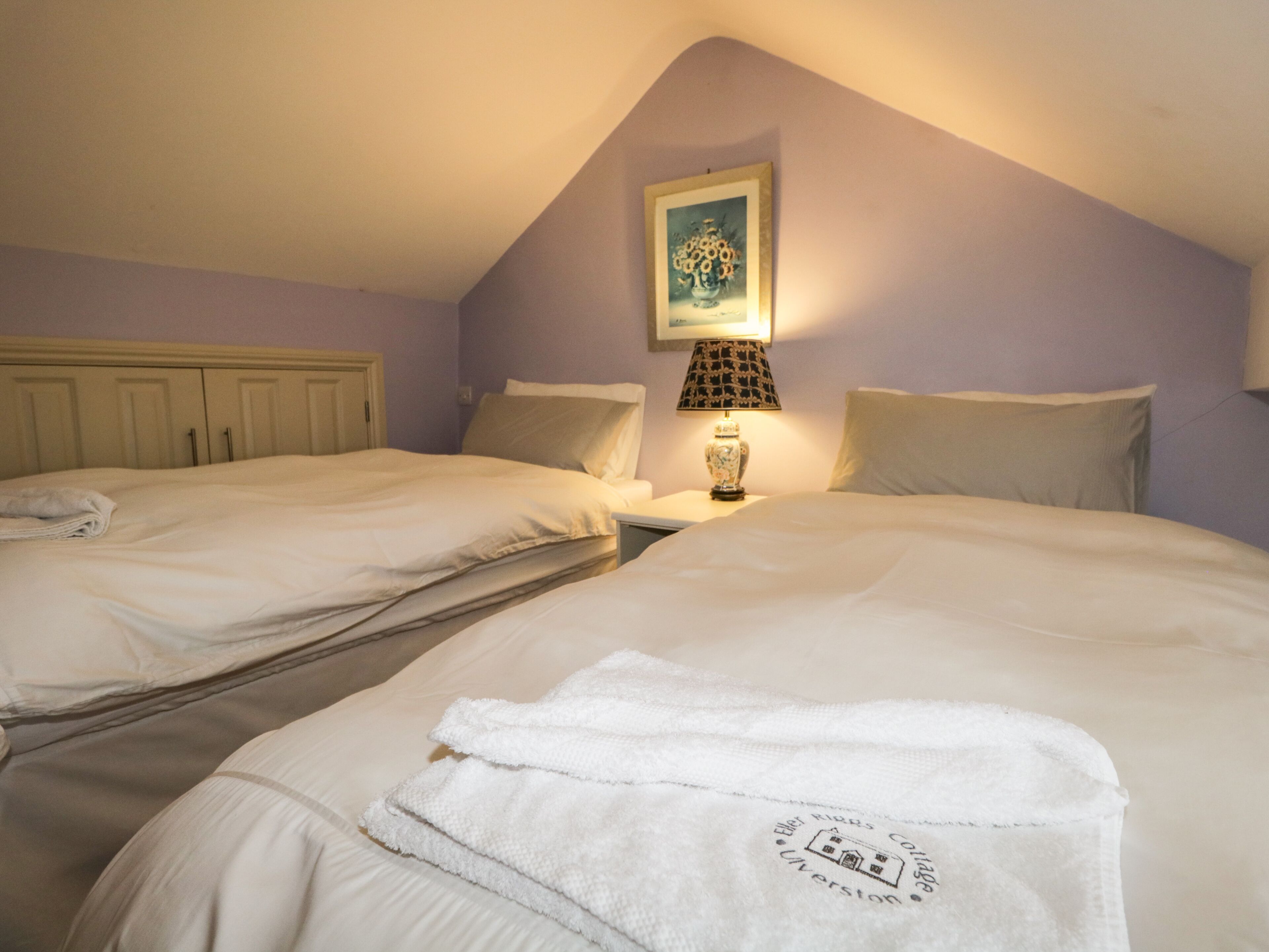 A hotel room with two beds, a nightstand with a lamp, and a painting on the wall.