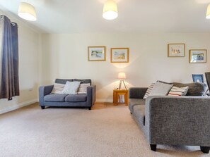Ein Wohnzimmer mit zwei grauen Sofas, einem kleinen Holztisch mit Lampe und gerahmten Bildern an der Wand.