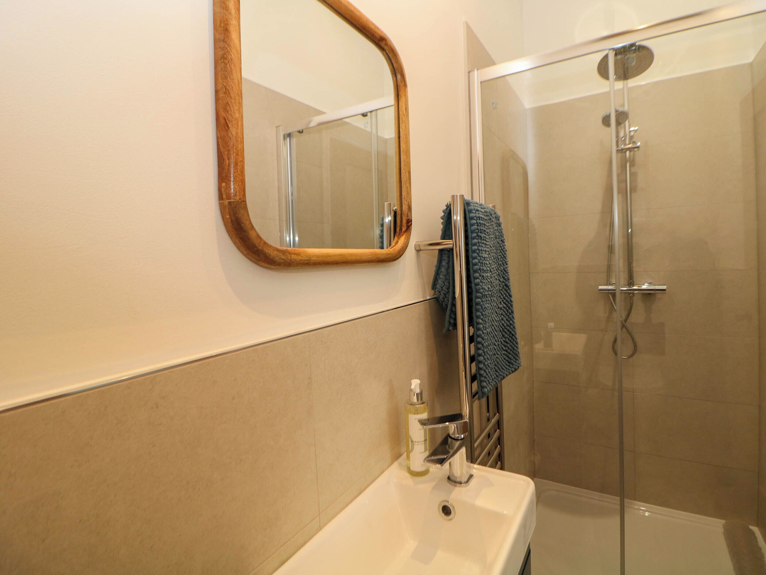 Une salle de bain avec un lavabo blanc, un miroir encadré en bois et une douche fermée par des parois de verre.