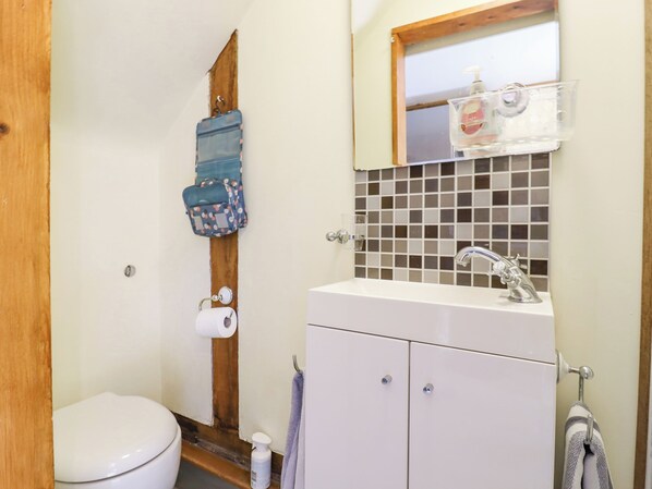 A bathroom with a white toilet, a sink with a mirror above it, and a towel rack. - The Studio, Horseshoe Cottage (Cambridge)