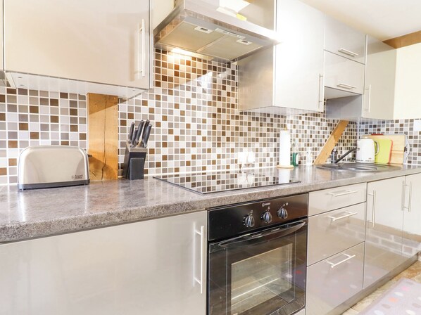 A modern kitchen with a built-in oven, stainless steel appliances, and a tiled backsplash. - The Studio, Horseshoe Cottage (Cambridge)