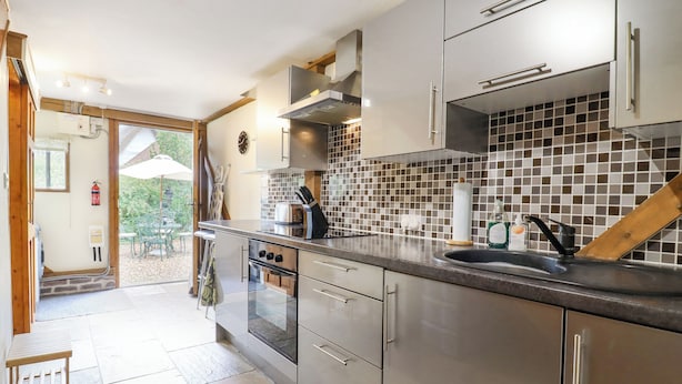 A modern kitchen with stainless steel appliances, a tiled backsplash, and a view to an outdoor patio. - The Studio, Horseshoe Cottage (Cambridge)