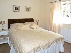 A neatly made bed with a headboard, two bedside lamps, and two framed pictures on the wall. - Braewood (Inverness)