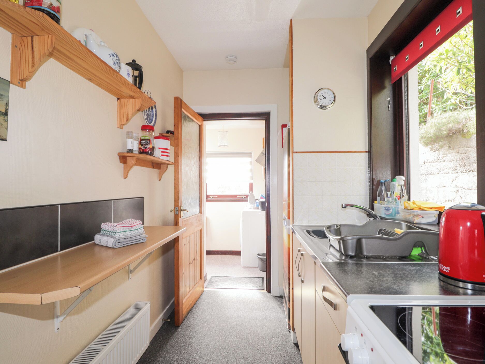 A compact kitchen with a sink, a red kettle, and a window with a view of greenery.