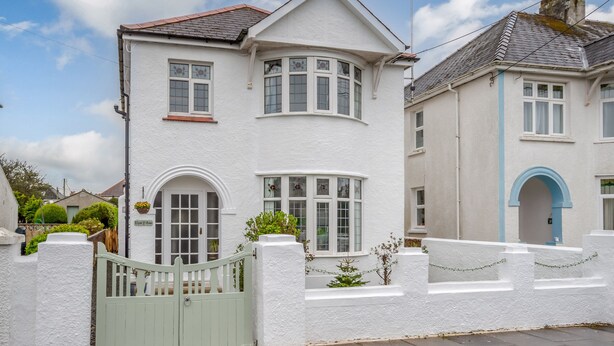 A two-story white house with a green gate, a small garden, and a clear sky. - Llys-y-gân (Fishguard)