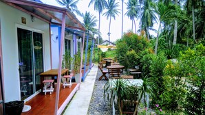 A covered outdoor seating area with tables and chairs, surrounded by lush greenery and palm trees. - Baan Suchanuch (Don Sak)