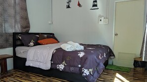 A neatly made bed with a floral duvet, a wooden nightstand, and a green rug on a wooden floor.