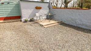 A patio area with a table and chairs, a small garden with potted plants, and a white wall. - Ffynnon Tom (Haverfordwest)
