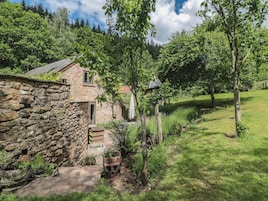 Uma casa de pedra com um pequeno jardim, cerca de madeira e gramado.