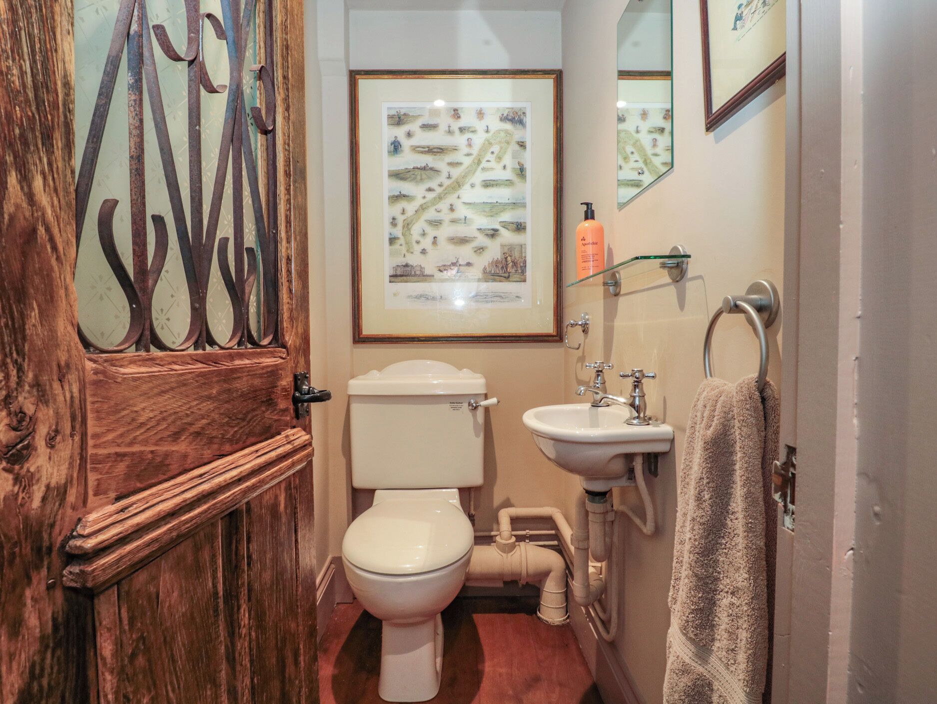 Un baño con puerta de madera, inodoro, lavamanos y toallero.