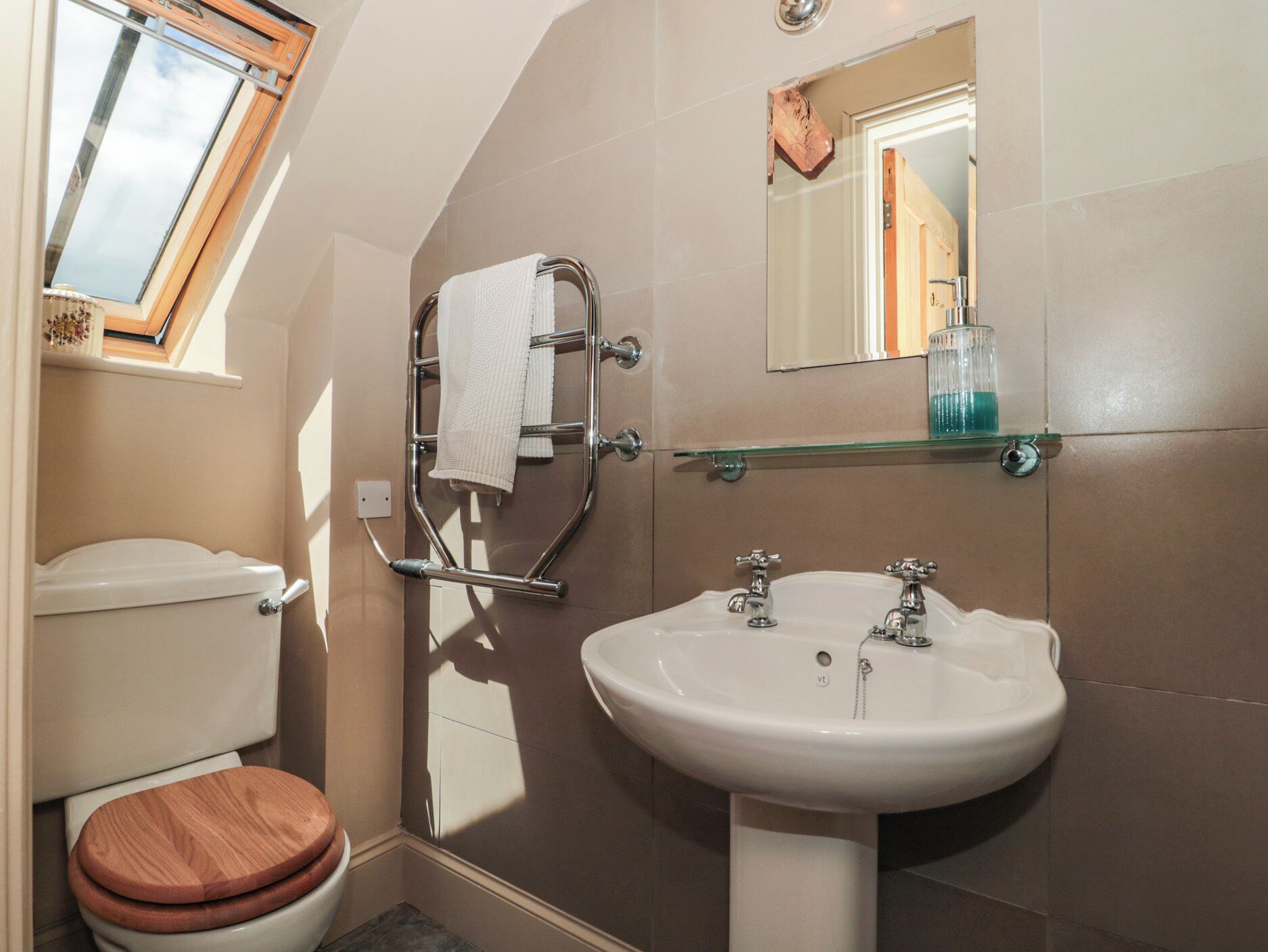 A bathroom with a toilet, a sink, a towel rack, a mirror, and a window.